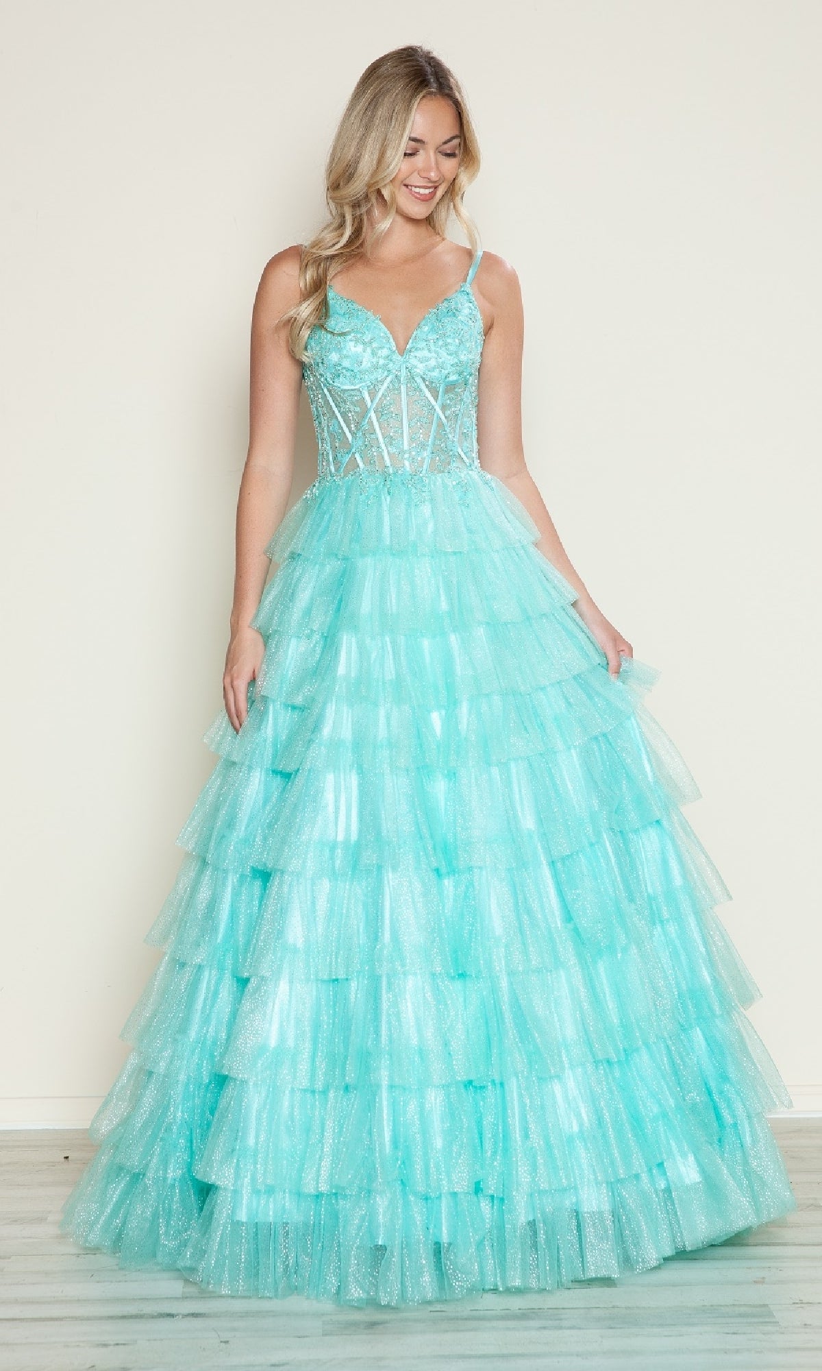 A woman models the Poly USA 9608 long prom dress, featuring a sleeveless light blue ruffled gown with a fitted lace corset bodice and flowing tiered tulle skirt, set against a plain light-colored wall.